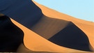Sossusvlei-Dünen in der Namib-Wüste, eine Wüste direkt am Meer. Küstenwüsten befinden sich in der Nähe von kalten Ozeanströmungen aus der Antarktis. Kühle Luft kann wegen warmer Passatwinde nicht aufsteigen, Wolken und Regen bleiben aus. | Bild: picture-alliance/dpa