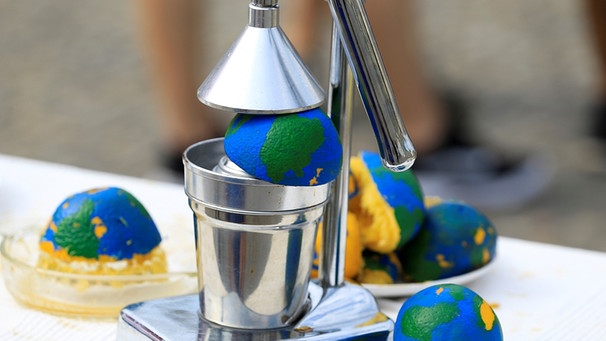 Zu sehen sind als Planet Erde angemalte Orangen in einer Saftpresse. Was ist der Earth Overshoot Day? Wie wird der Welterschöpfungstag berechnet?  Und wie können wir unseren ökologischen Fußabdruck verbessern? Hier erfahrt ihr mehr. | Bild: picture-alliance/dpa